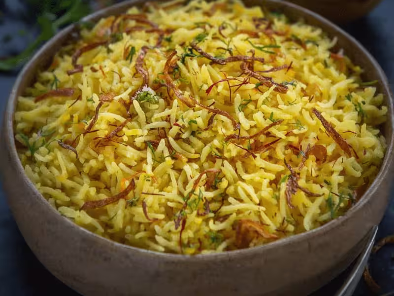 Bowl of saffron rice with long basmati grains golden color saffron threads and herbs on top showing a freshly prepared homemade saffron rice dish..